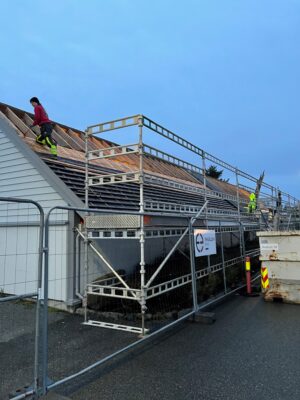 Bilde av carporten på Årabrot som ble revet for å gi plass til nybygget. Det er rigget stillas på siden, og to stykker står og plukker ned skifer til gjenbruk fra taket.