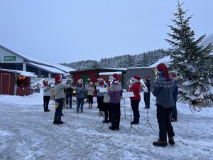 Haugesund ungdomskors er avbildet mens de spiller på julemarkedet. Det er snø, og vi ser et stort juletre og juleboder i bakgrunnen.